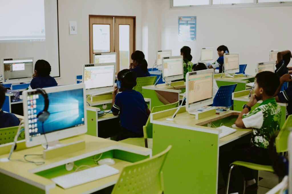 Children learning in a modern computer lab environment with headphones and desktops.