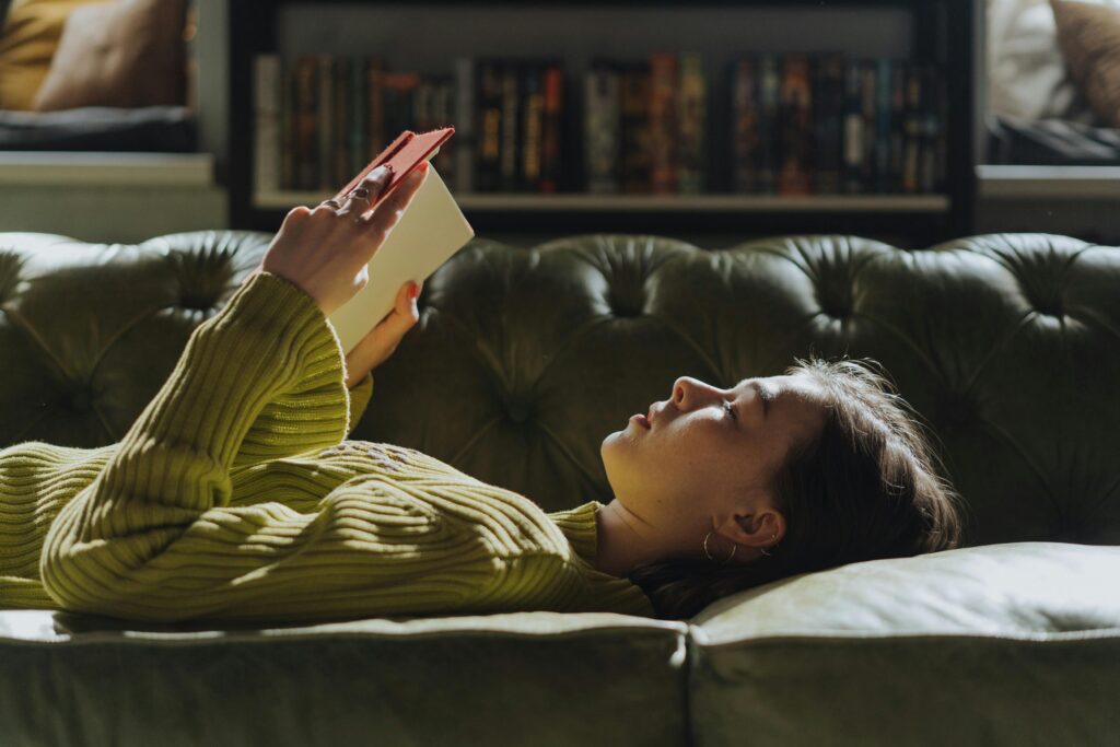 A young woman lies on a sofa reading a book, enjoying a peaceful indoor moment.